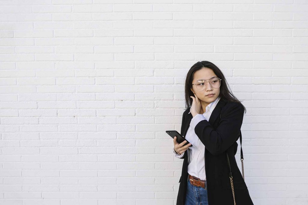 Portrait of young businesswoman with mobile phone standing in front of white wall